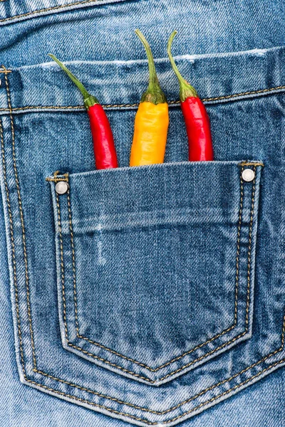 Pocket of jeans staffed with red and yellow chilly peppers, denim background. Peppers in back pocket of blue jeans. Hot sensations concept. Piquant secret in pocket of pants