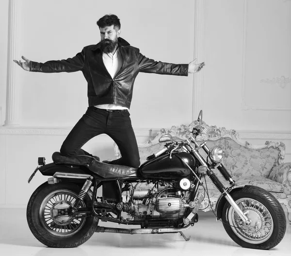 Man biker in leather jacket near motor bike in luxury living room interior background. Hipster biker brutal in leather jacket on motorcycle enjoying richness. Superiority concept