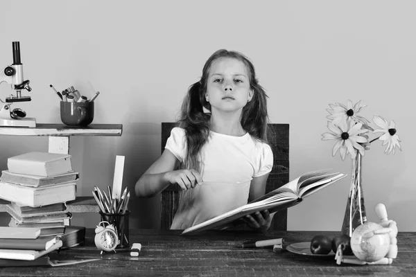 Geri okul kavramı. Kız öğrenci masa başında ciddi bir yüz tutan kitap ile oturuyor.