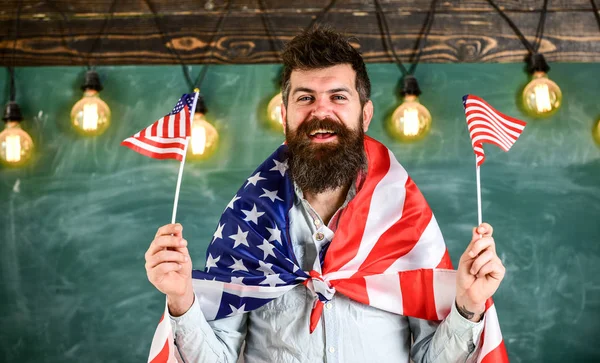 Amerikan bayrakları ile Amerikalı öğretmen dalgalar. Vatansever eğitim kavramı. Öğrenci değişim programı. Sakal ve bıyık mutlu yüz tutan bayrakları ABD, sınıfta, arka plan kara tahta üzerinde olan adam