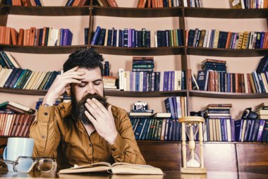 Öğretmen ya da sakal Kitaplığı'nda eğitim ile öğrenci. Esneme yüz kitap okumak, ders, kitap rafı arka plan üzerinde adam. Adam, kupa ve kum saati ile masada oturur. Kendi eğitim kavramı