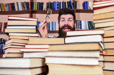 Kazık kitap kütüphane, kitap rafı arka plan üzerinde arasında mutlu yüz kişi. Öğretmen ya da öğrenci sakallı gözlük takmaz, defocused kitaplar ile masada oturur. Bilimsel araştırma kavramı
