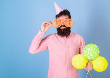 Gülümseyen adam partide, mutluluk kavramı eğleniyor büyük bardaklarda sakallı. Hipster sakal ve bıyık mavi zemin üzerine pembe gömlekli adam. Sanatçı oyuncak balon ile poz Doğum günü şapkalı