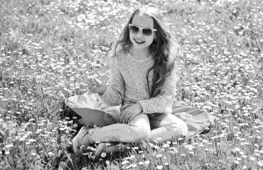 Alt dudakları çayır fotoğraf oturumunda için gülümseyen güneş gözlüğü karton ile poz. Kız grassplot, arka planı yeşil çimlere oturur. Kız neşeli yüzü açık açık havada eğlence harcamak. Fashionista kavramları