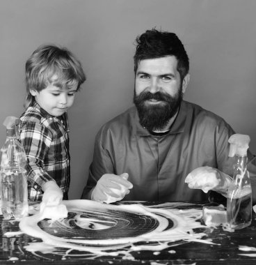 Baba oğul ve yeşil zemin üzerine temizlik malzemeleri ile. Baba ve çocuk köpük masanın üzerine yaptı. Aile zaman kavramı.