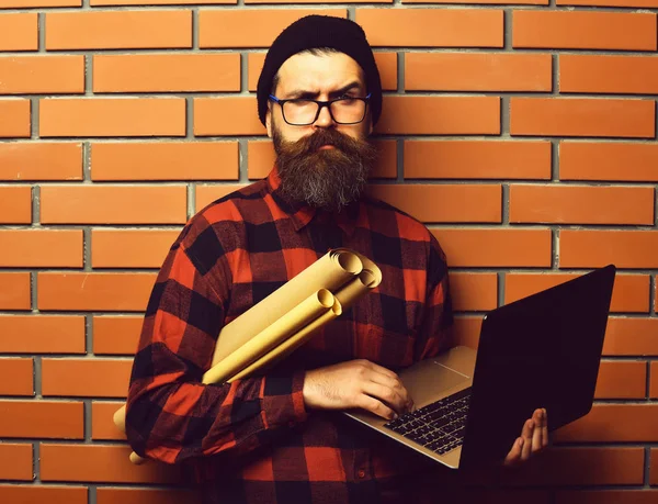 Bearded brutal caucasian hipster holding laptop and craft paper — Stock Photo, Image