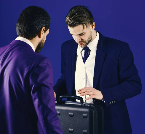 Männer in Anzügen oder Geschäftsleute treffen sich zur Übergabe schwarzer Aktentaschen. Geschäftspartner mit geschäftigem Gesicht auf blauem Hintergrund. — Stockfoto