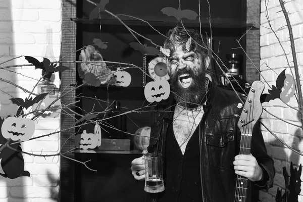 Halloween decor on background Demon with horns and wild face holds black electric guitar.