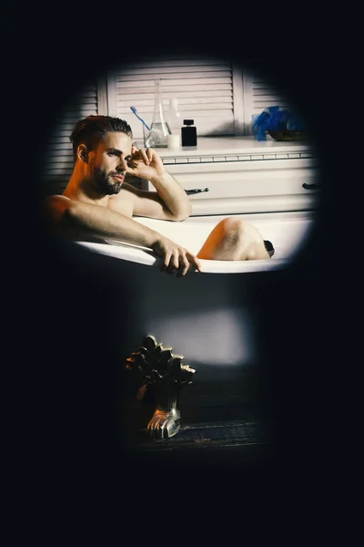 Guy in bathroom with toiletries on background. Sex and relaxation concept. Man with beard and dreamy face. Macho sitting naked in bathtub with dreamy face — Stock Photo, Image