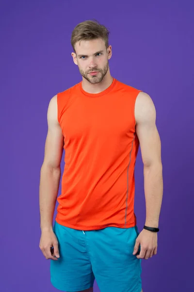 Deportista sobre fondo violeta. Hombre musculoso en chaleco naranja y pantalones cortos azules. Ajuste y confianza. Moda deportiva para entrenamiento y entrenamiento. Entrenador personal para un estilo de vida saludable. Fitness y bienestar. — Foto de Stock