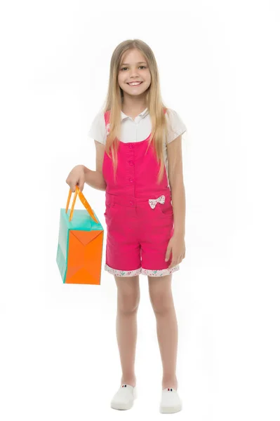 Szczęśliwa dziewczyna z torbą na zakupy na białym tle. Mała dziewczynka zakupoholiczki uśmiech z worka papierowego. Dziecko shopper w kombinezon mody. Przygotowania do Świąt i uroczystości. Dzieciństwa. Zakupy i sprzedaż — Zdjęcie stockowe