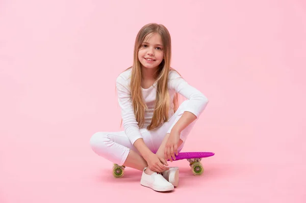 Niño feliz sentarse en el tablero de peniques sobre fondo rosa. Chica sonrisa con monopatín. Patinadora lista para montar. El monopatín es divertido. Pasatiempo activo y actividad deportiva, tendencia pastel punzante. Infancia — Foto de Stock