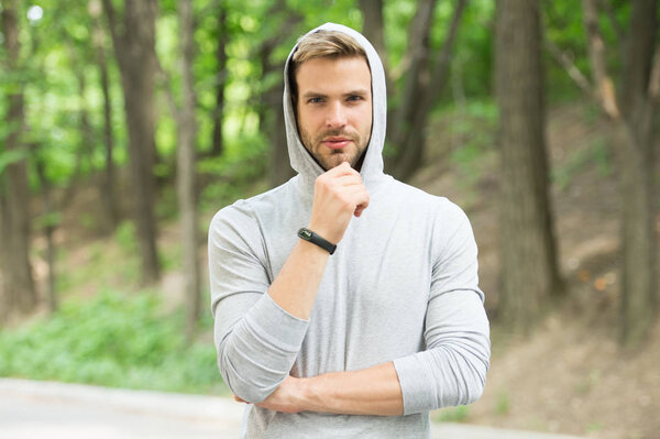 Bearded man in hood on natural landscape. Confident sportsman in casual style, fashion. Relax in forest or park. Ready for workout. Training on fresh air. Sport and fitness