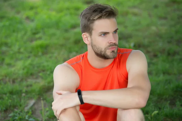 Atleta llevar pulsera podómetro en la mano. Hombre atlético relajarse en la hierba verde. Comprobando los resultados del entrenamiento. Las tecnologías facilitan la formación. Hombre musculoso en verano. Mantener el ojo en el tiempo — Foto de Stock