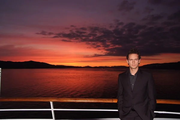 Mann steht an Deck eines Schiffes am dramatischen Himmel über dem Meer im norwegischen Bergen. Geschäftsleute genießen die Schifffahrt am Abend. Geschäfts- oder Urlaubsreise. Sommerurlaub am Meer. Abenteuer und Fernweh. Sonnenuntergang oder Sonnenaufgang. — Stockfoto