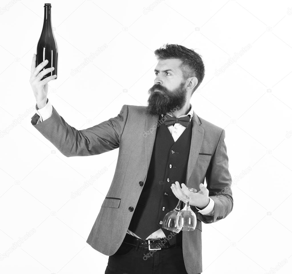 Wine tasting, wine waiter, perfect service concept. Sommelier with serious face proposes drink. Sommelier with elegant suit, bow tie and handsome face. Mature man holds wineglasses and bottle of wine.