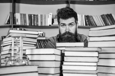 Kitaplığı'nda, eğitim sırasında kitaplar, kitap rafı arka plan üzerinde yığınları arasında sakin yüz kişi. Kazık kavramı. Öğretmen ya da öğrenci sakallı defocused kitaplar ile masada oturur