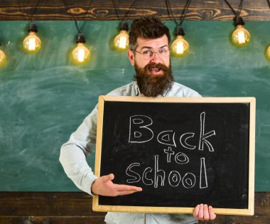 Geri okul kavramı. Adam sakal ve bıyık neşeli yüzü memnuniyetle öğrencilerin, kara tahta arka plan ile. Gözlük öğretmen blackboard yazıt ile geri okula tutar