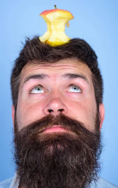 Adam yakışıklı hipster uzun sakal neredeyse kafasına elma güdük hedef olarak yem. Canlı hedef kavramı. Hipster sürpriz elma güdük hedef üzerinde kafa mavi arka plan, yüz kadar yakın. Kilo kaybı gol