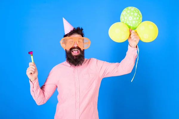 Mann mit Bart und Schnurrbart auf glücklichem Gesicht hält Luftballons, blauer Hintergrund. Hipster mit Riesenbrille feiern Geburtstag. Mann im Partyhut mit Feiertagsattributen feiert. Parteikonzept — Stockfoto