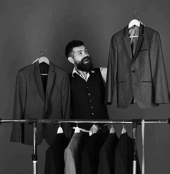 Official wardrobe choice concept. Man with beard by clothes rack. Businessman with happy face