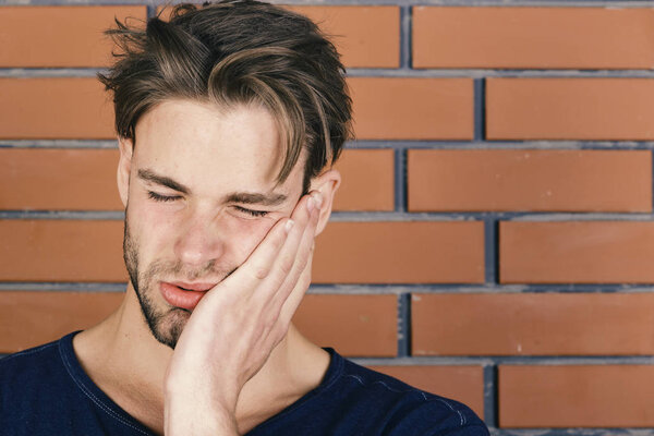 Мачо со страждущим лицом держит руку за щеку