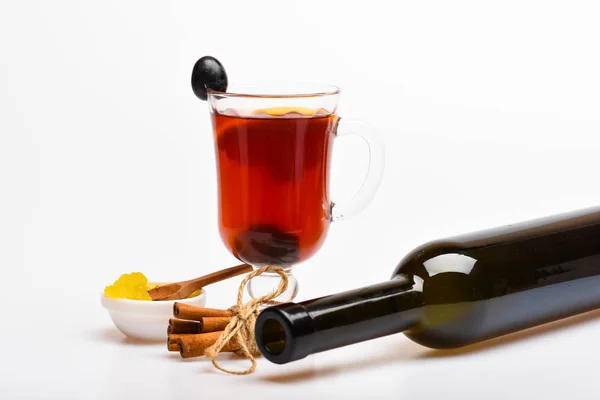 Verre avec vin chaud avec raisin et cannelle et bouteille de vin. Concept de boissons saisonnières. Verre avec vin chaud ou boisson chaude au raisin, cannelle et miel, fond blanc, gros plan — Photo