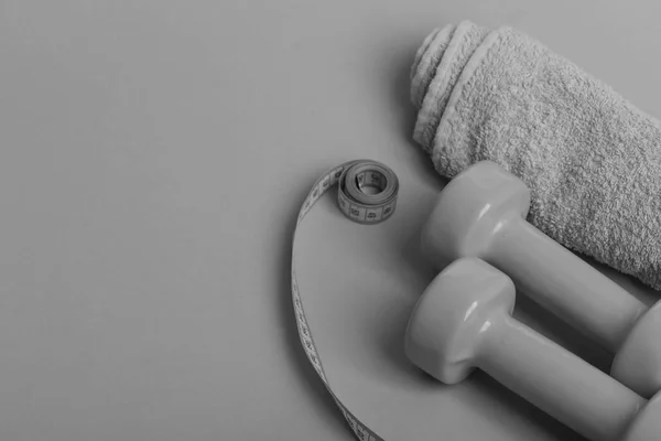 Dumbbells in bright green color, measure tape roll and towel on green background. Tape measure in cyan color by lightweight barbells, copy space — Stock Photo, Image