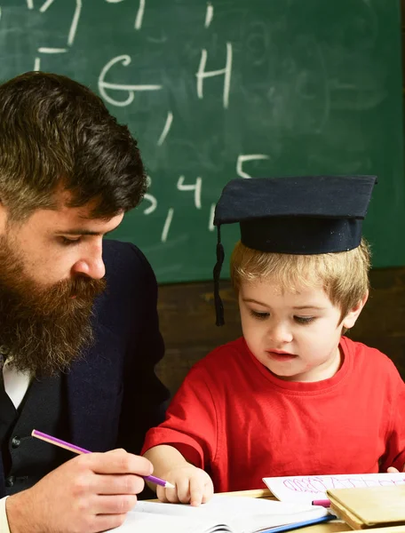 先生と勉強熱心な子供。正式な摩耗と鏝板の教室で、背景に黒板に生徒の教師。少年は、するのに役立ちます、宿題のチェックの父の息子。ホーム スクーリングのコンセプト — ストック写真