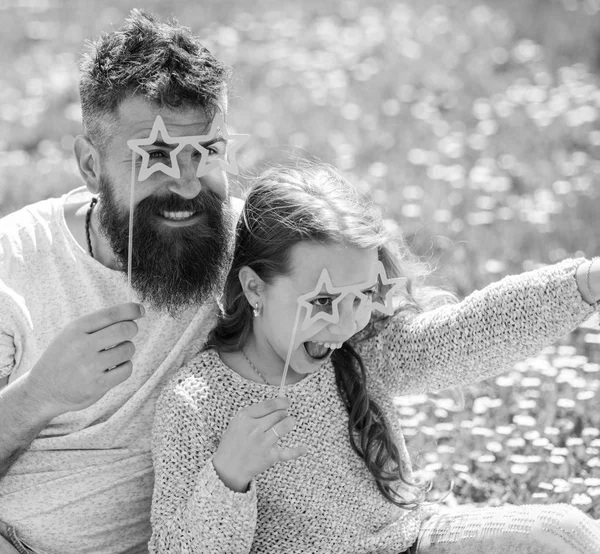 Família passar o lazer ao ar livre. O pai e a filha sentam-se na relva no campo, fundo verde. Criança e pai posando com estrela em forma de óculos atributo cabine de foto no prado. Conceito de estrela e fama — Fotografia de Stock