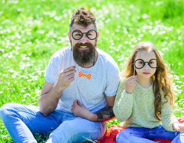 O pai e a filha sentam-se na relva no campo, fundo verde. Criança e pai posando com óculos atributos de cabine de fotos no prado. Conceito inteligente e inteligente. Família passar o lazer ao ar livre — Fotografia de Stock