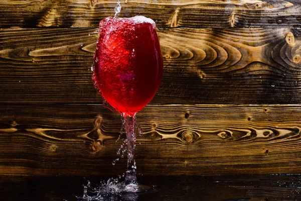 Cam şarap dökme sıvı sıçraması ve su damlaları ile. Bardağı su koyu ahşap zemin fışkırmaları ile doldurma. Serinletici içecek konsepti