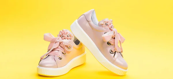 Comfortable footwear concept. Cute shoes on yellow background. Footwear for girls or women decorated with pearl beads. Pair of pale pink female sneakers with velvet ribbons — Stock Photo, Image