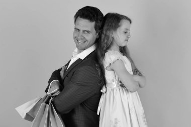 Kız ve erkek gülümseyen yüzler ile arka arkaya stand ve alışveriş torbaları, pembe arka plan tutun. Liseli kız ve baba alışveriş yapmak. Baba ve kızı hediye satın