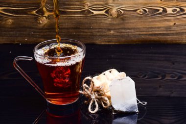 Su damlaları ve su damlalarıyla doldurulmuş çay bardağı. Çay demleme konsepti. Bardaklar suyla doluyor ya da koyu ahşap zemin üzerine su sıçrıyor. Fincan, çay poşeti ve kurabiyeler masada.