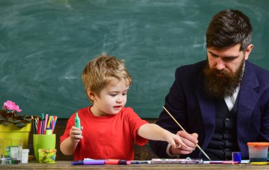 Sakallı öğretmeni, sınıfta, kara tahta arka plan çizmek için küçük oğlu baba öğretir. Sanat ders kavramı. Yetenekli sanatçı oğlu ile vakit geçirmek. Çocuk ve resim öğretmeni meşgul yüz boyama,