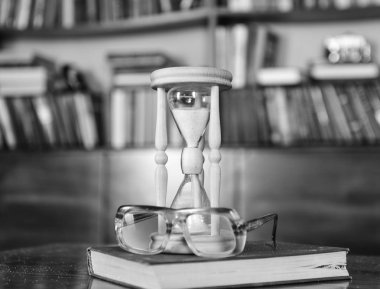 Kum saati, eski kitap ve ahşap masa, Kütüphane arka plan üzerinde gözlük. Bilim adamları öznitelikleri kavramı. Eski moda gözlük yakın zaman sayma kum saati. Kum kum saati içinde düşme