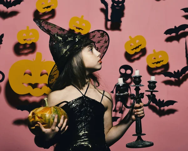 Halloween feest en decoraties concept. Kind in heksen kostuum houdt pompoen en kroonluchter. — Stockfoto