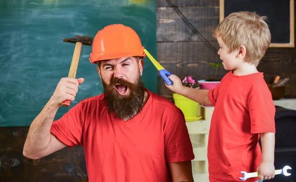 Babalık kavramı. Baba, üst koruyucu kask okul atölyesinde farklı araçları kullanmak için küçük oğlu öğretim içinde sakallı. Evlat, çocuk oyuncakla oynamak neşeli, öğrenme kullanım araçları ile baba gördüm