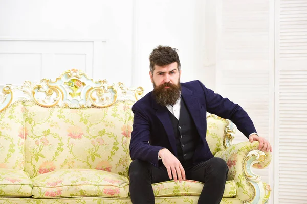 Hombre con barba y bigote con traje clásico, elegante atuendo de moda. Macho atractivo y elegante en serio, cara pensativa sentado en el sofá de lujo a la antigua. Concepto de masculinidad —  Fotos de Stock