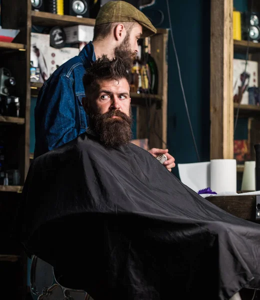 Hipster client getting haircut. Haircut process concept. Man with beard covered with black cape waiting while barber changing clipper grade. Client with beard ready for trimming or grooming