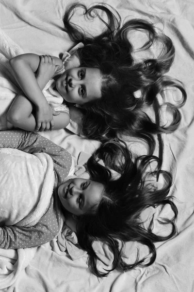 Çocuklar mutlu yüzler ve kalp şeklinde saç ile yatakta dinlenin. Çocukluk ve sevgi kavramı. Kızlar beyaz ve pembe levhalar üzerinde — Stok fotoğraf