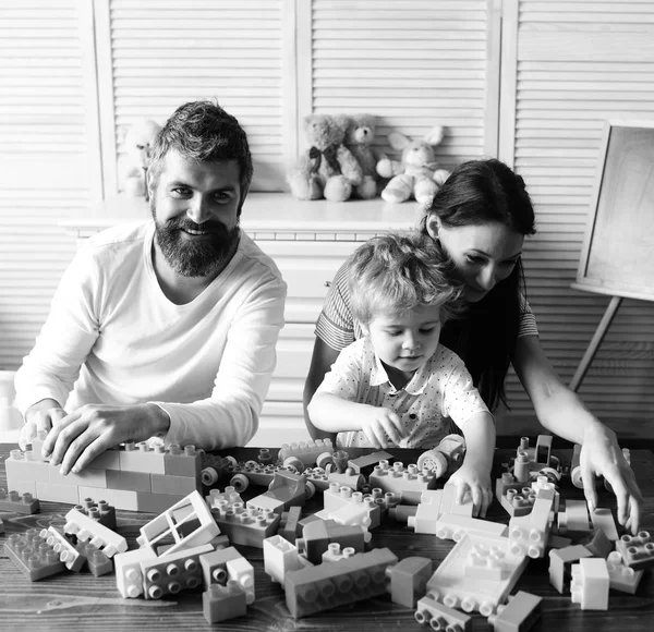 Mamá, papá y niño con juguetes sobre fondo de madera construidos a partir de bloques. Amor y concepto de juegos familiares. Familia joven pasa tiempo —  Fotos de Stock