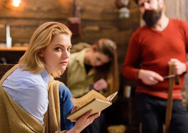 Blond woman with suspicious look reading book. Female in blue shirt and jeans warming up with beige woolen blanket. Family spending time together. Girl fond of literature, bookworm enjoying new novel — Stock Photo, Image