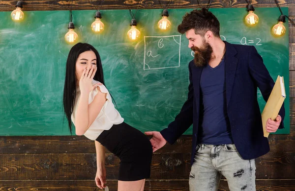 Schoolmaster punishes sexy student with slapping on her buttocks. Man with beard slapping sexy student, chalkboard on background. — Stock Photo, Image