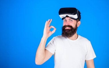 Adam uzun sakallı ve Ok jest gösterilen mutlu yüzünde geniş bir gülümseme ile. Sakallı enginner Vr kulaklık, dijital ilerleme kavramı, yeni modeli sınama. Üzerinde mavi arka plan izole trendy sakallı hippi