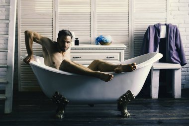 Seks ve gevşeme kavramı. Sakal ve baştan çıkarıcı yüzü olan adam. Banyo tuvalet malzemeleri, sandalye ve arka plan merdivenlerde adam