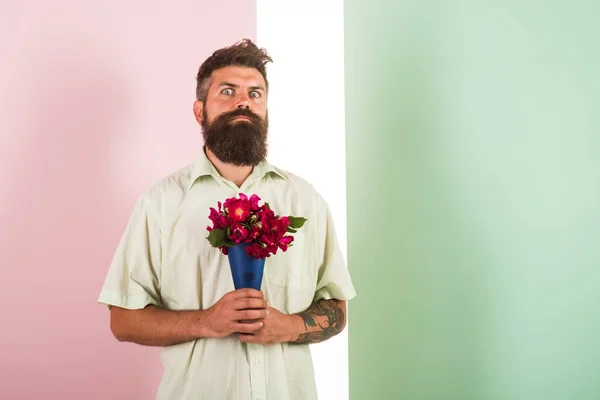 Flowers delivery concept. Man with beard surprised grimace holds bouquet fresh flowers. Delivery man with flowers. Hipster with beard ready holiday congratulate. Guy holds bouquet nervous about date