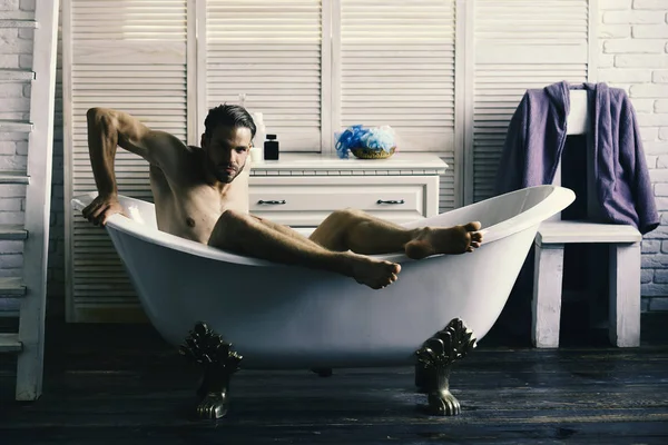 Seks ve gevşeme kavramı. Sakal ve baştan çıkarıcı yüzü olan adam. Banyo tuvalet malzemeleri, sandalye ve arka plan merdivenlerde adam