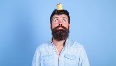 Canlı hedef kavramı. Adam yakışıklı hipster uzun sakal neredeyse kafasına elma güdük hedef olarak yem. Hipster yüz elma güdük hedef üzerinde kafa mavi arka plan, kopya alanı ile şaşırttı. Kilo kaybı gol